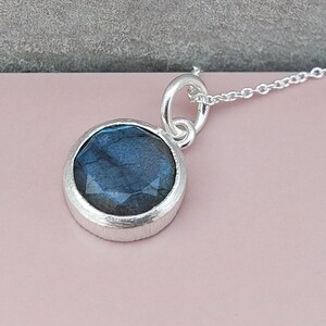 May include: A silver necklace with a round pendant featuring a blue labradorite gemstone.