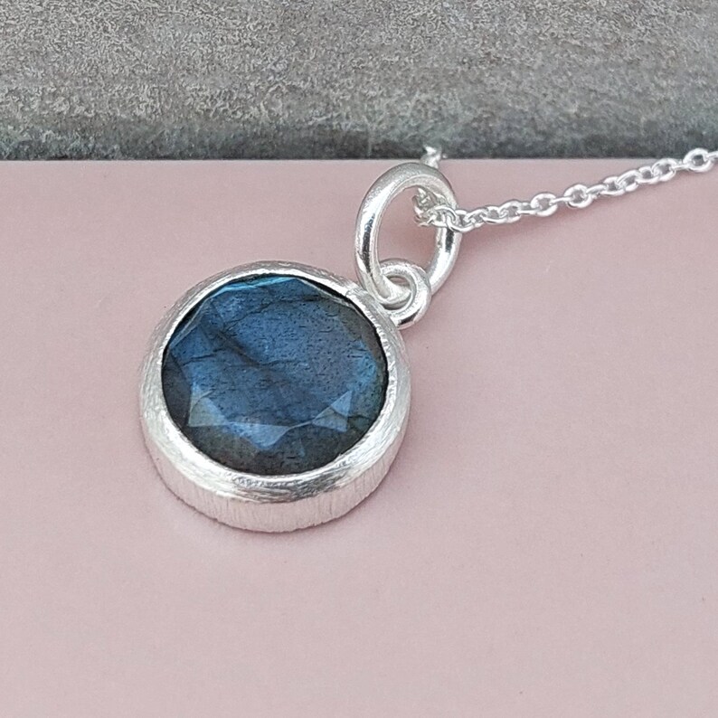 May include: A silver necklace with a round pendant featuring a blue labradorite gemstone.