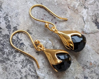 Puede incluir: Un par de pendientes de oro con gotas de piedras preciosas negras. Los pendientes tienen un diseño floral delicado.