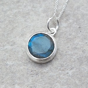 May include: A silver necklace with a round pendant featuring a blue labradorite gemstone.