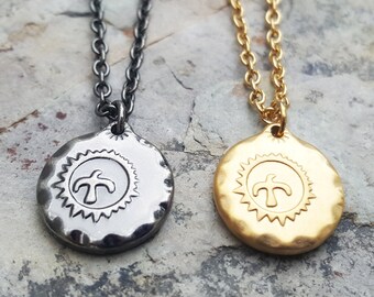 Puede incluir: Dos collares con un colgante redondo que presenta una palmera estilizada dentro de un diseño de sol radiante. Un collar tiene una cadena y un colgante plateados, el otro tiene una cadena y un colgante dorados.