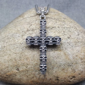 May include: A silver skull cross pendant necklace. The cross is made up of multiple skulls, with a single skull at the top.