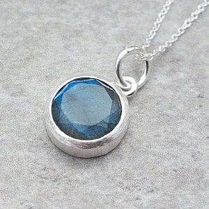 May include: A silver necklace with a round pendant featuring a blue labradorite gemstone.