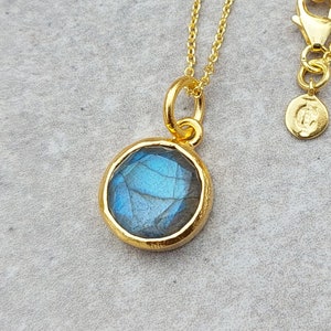 May include: Gold necklace with a round blue labradorite gemstone pendant.