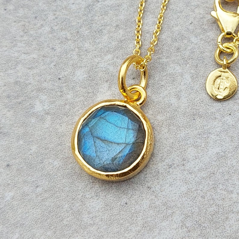May include: Gold necklace with a round blue labradorite gemstone pendant.