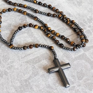 May include: A necklace with a black cross pendant. The necklace is made of tiger's eye and hematite beads.