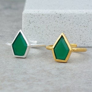 May include: Two adjustable rings with a green gemstone in a geometric shape. One ring is silver and the other is gold.