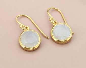 May include: A pair of gold earrings with round moonstone gemstones. The earrings have a simple, elegant design.