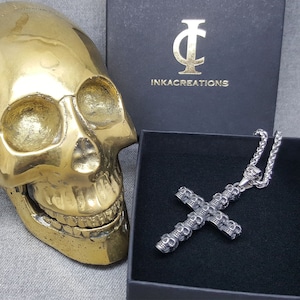 May include: A silver skull cross pendant necklace with a silver chain. The necklace is in a black box with the text "INKACREATIONS" on the lid.