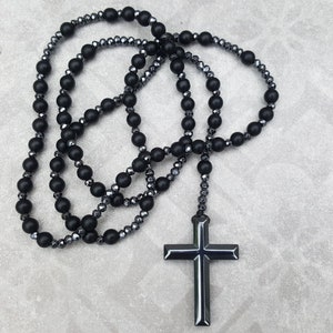 May include: A black beaded necklace with a black cross pendant. The necklace is made of multiple strands of beads, some of which are faceted.