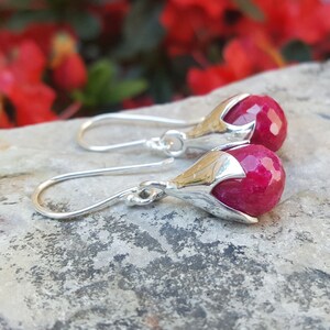 May include: A pair of silver dangle earrings with a pink gemstone set in a flower-shaped setting.
