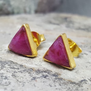 Könnte beinhalten: Ein Paar goldene Dreiecksohrringe mit rosafarbenen Edelstein-Akzenten.