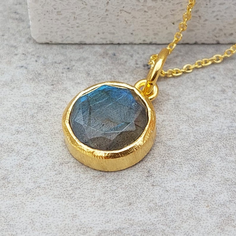 May include: A gold necklace with a round labradorite gemstone pendant. The pendant has a textured gold bezel.