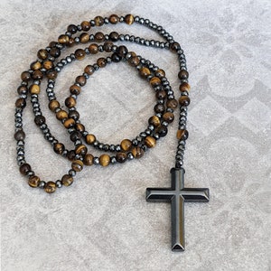 May include: A beaded necklace with a black cross pendant. The necklace is made of tiger's eye and hematite beads.