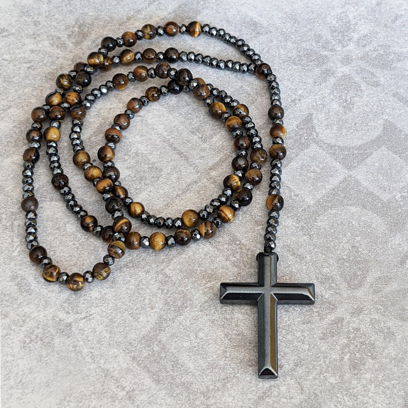 May include: A beaded necklace with a black cross pendant. The necklace is made of tiger's eye and hematite beads.