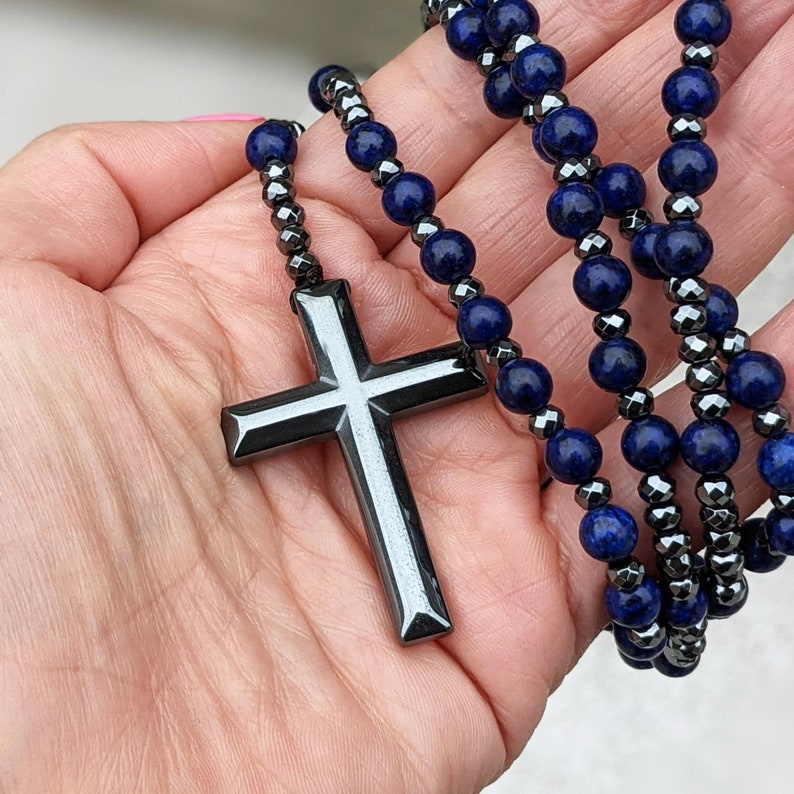 May include: A black hematite and lapis lazuli beaded necklace with a large, silver-toned cross pendant.