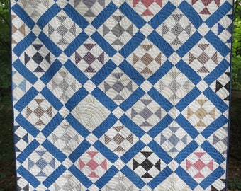 Könnte beinhalten: Eine blaue und weiße Steppdecke mit einem Rautenmuster. Jede Raute ist mit einem anderen Stoff gefüllt, darunter Karo, Gingham und Uni-Farben. Die Steppdecke ist mit einem wellenförmigen Muster gesteppt.