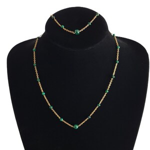 Peut inclure: Un collier et un bracelet en chaîne dorée avec des perles de pierres précieuses vertes. Le collier et le bracelet sont présentés sur un présentoir en velours noir.