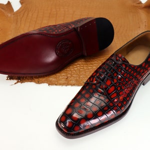 May include: A pair of red and black leather dress shoes with a crocodile pattern. The shoes have a lace-up closure and a pointed toe.
