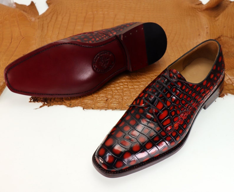 May include: A pair of red and black leather dress shoes with a crocodile pattern. The shoes have a lace-up closure and a pointed toe.