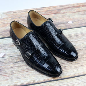 May include: A pair of black leather dress shoes with a crocodile pattern. The shoes have two buckles on each shoe.