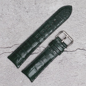May include: A dark green watch strap featuring a glossy finish and a textured crocodile-style embossed pattern. The strap includes a silver-toned metal buckle and multiple adjustment holes for securing the band to a wrist.