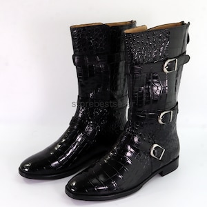 May include: A pair of black leather boots with a crocodile pattern and three silver buckles. The boots have a pointed toe and a low heel.