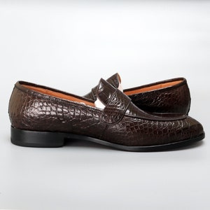May include: A pair of brown leather loafers with a crocodile pattern. The loafers have a slip-on design and a rounded toe.