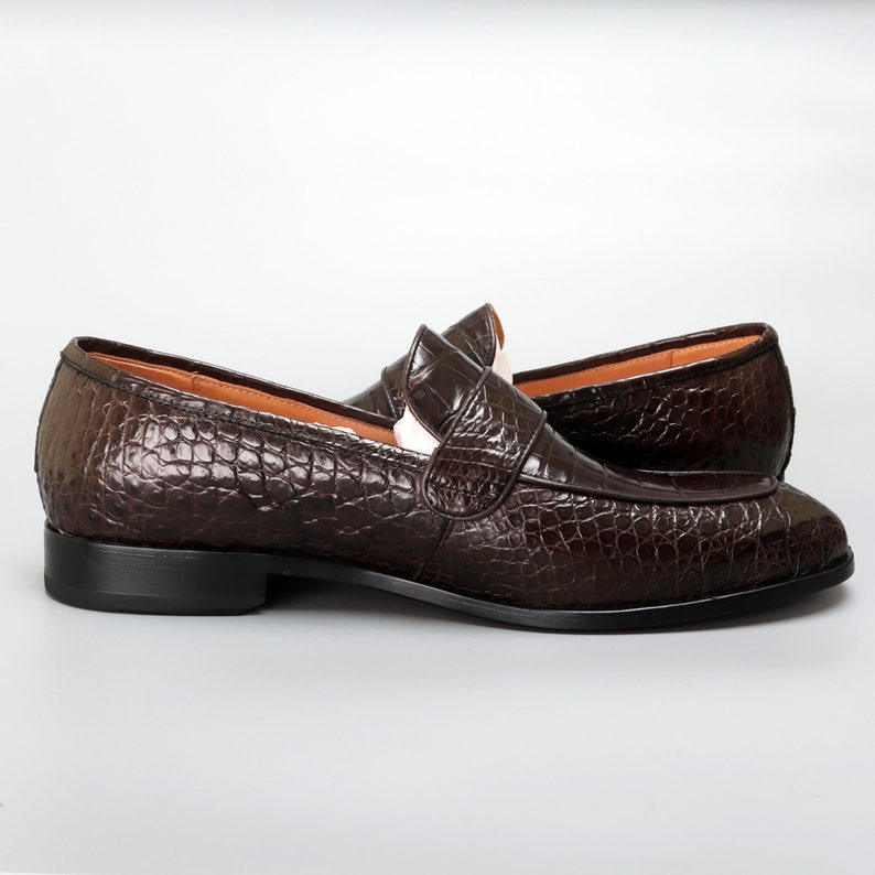 May include: A pair of brown leather loafers with a crocodile pattern. The loafers have a slip-on design and a rounded toe.