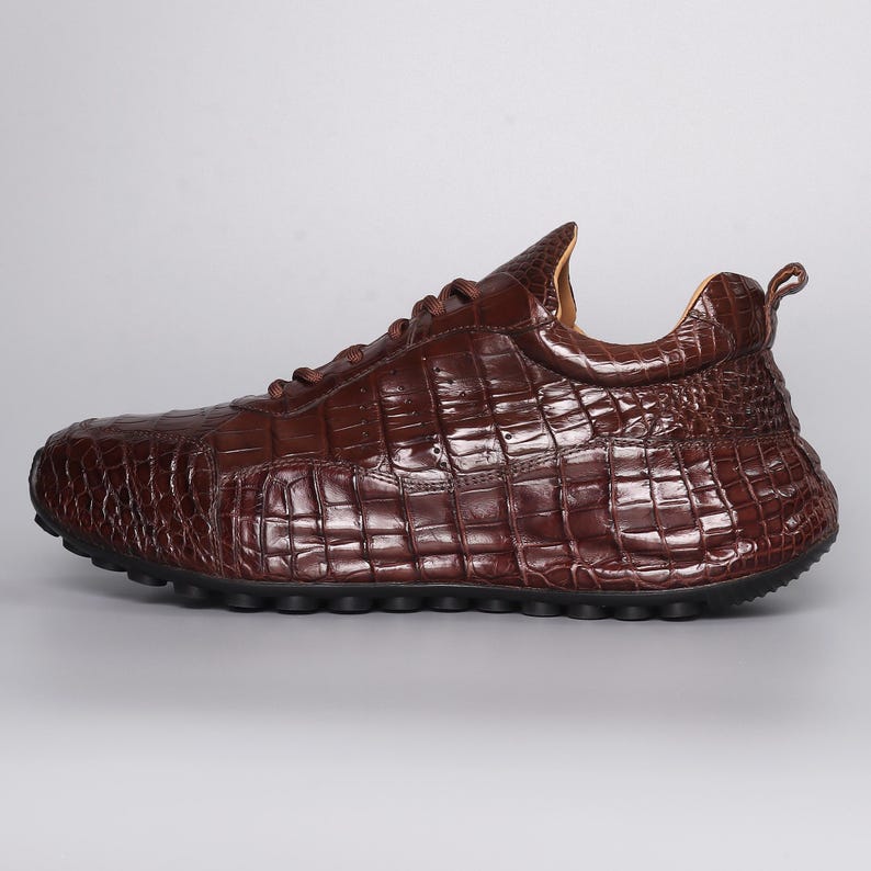 Puede incluir: Zapatilla de cuero marr&oacute;n con textura de piel de cocodrilo. El zapato tiene una puntera redondeada, cierre de cordones y suela gruesa. El empeine presenta un patr&oacute;n texturizado y en relieve.
