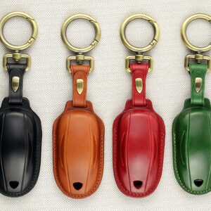 May include: Four leather keychains with different colored leather covers. The keychains are black, brown, red, and green. Each keychain has a gold metal ring and a gold metal clasp.