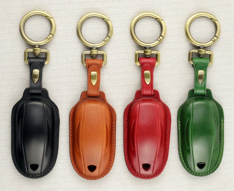May include: Four leather keychains with different colored leather covers. The keychains are black, brown, red, and green. Each keychain has a gold metal ring and a gold metal clasp.
