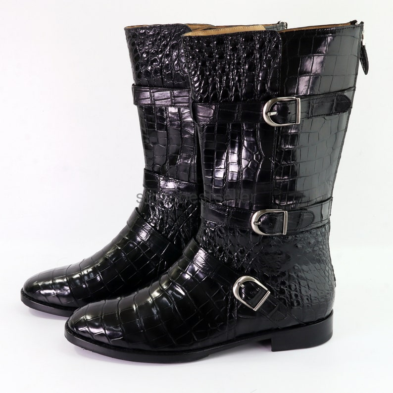 May include: Black leather boots with a crocodile pattern and multiple buckles. The boots have a pointed toe and a low heel.