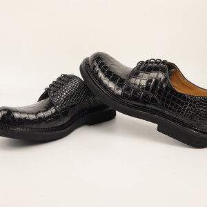 Left shoe angled to highlight the Alligator scale pattern, sleek silhouette, and polished black sole, set against a neutral background.