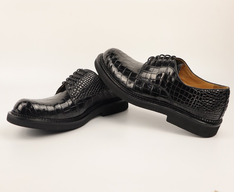 Left shoe angled to highlight the Alligator scale pattern, sleek silhouette, and polished black sole, set against a neutral background.
