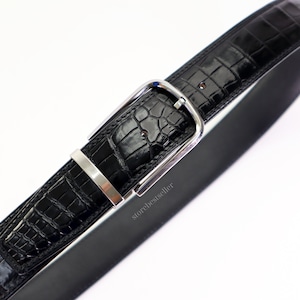 May include: A black alligator leather belt with a silver buckle. The belt is made of high-quality leather and has a classic design.