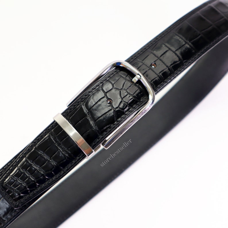 May include: A black alligator leather belt with a silver buckle. The belt is made of high-quality leather and has a classic design.