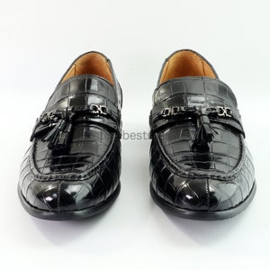 May include: A pair of black leather loafers with a crocodile pattern. The loafers feature a tassel detail and a chain accent.
