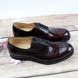 Peut inclure: Une paire de chaussures habill&eacute;es en cuir bordeaux &agrave; motif crocodile. Les chaussures ont des lacets et une pointe arrondie.