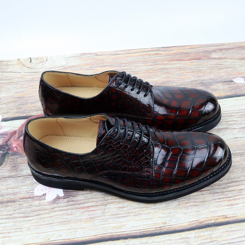 Peut inclure: Une paire de chaussures habill&eacute;es en cuir bordeaux &agrave; motif crocodile. Les chaussures ont des lacets et une pointe arrondie.