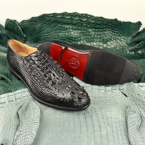 May include: A pair of black leather dress shoes with crocodile skin pattern. The shoes are on a green and blue crocodile skin background.