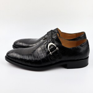 May include: Black leather dress shoes with a crocodile pattern and a silver buckle. The shoes have a pointed toe and a low heel.
