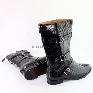 May include: Black leather boots with a crocodile pattern and multiple buckles. The boots have a pointed toe and a side zipper.