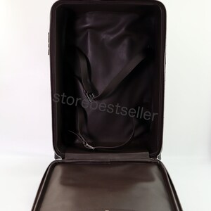 May include: Open brown leather suitcase with a zipper closure and a black interior. The suitcase has a strap system to secure items inside.