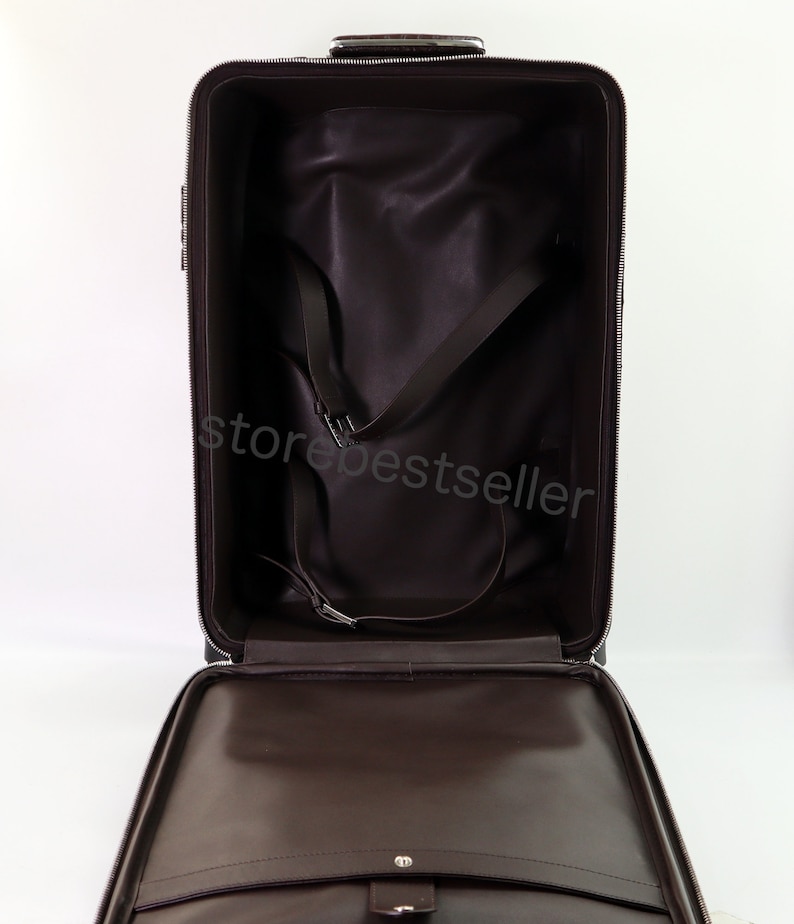 May include: Open brown leather suitcase with a zipper closure and a black interior. The suitcase has a strap system to secure items inside.