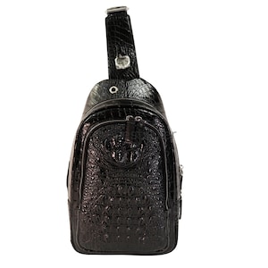 Könnte beinhalten: Eine schwarze Leder-Umhängetasche mit Kroko-Prägung. Die Tasche hat einen Reißverschluss und einen verstellbaren Schultergurt, der sich bequem an die Schulter anpassen lässt.