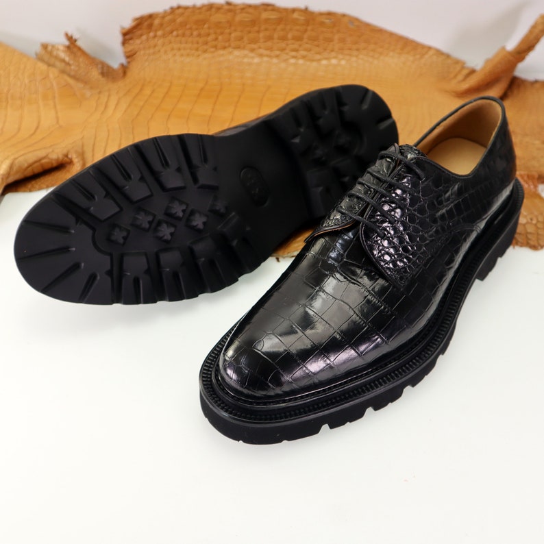May include: Black leather dress shoes with a crocodile pattern and a thick rubber sole.