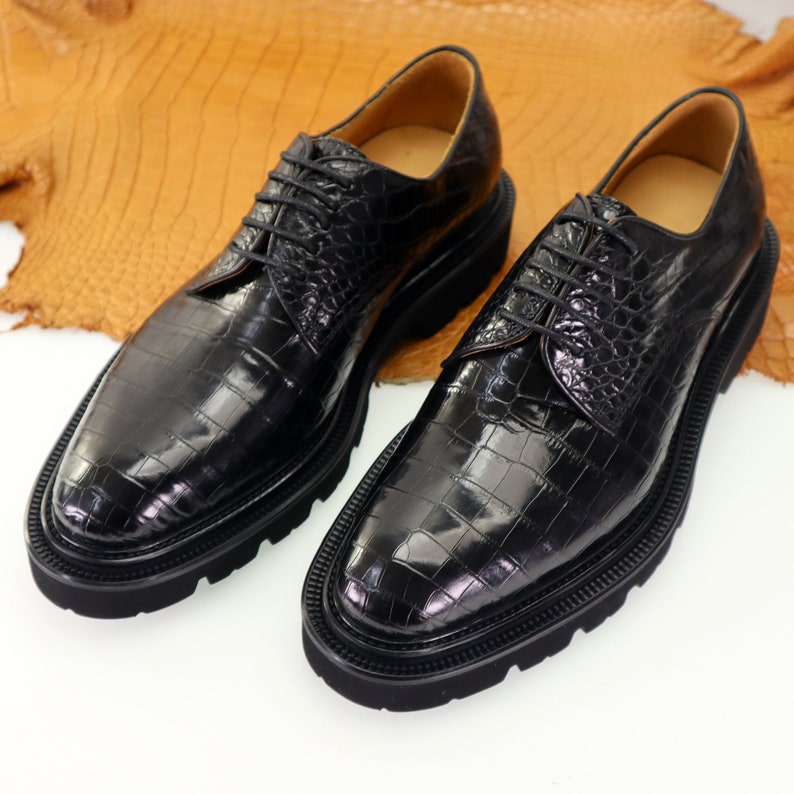 May include: A pair of black leather lace-up shoes with a crocodile pattern. The shoes have a thick rubber sole and a pointed toe.