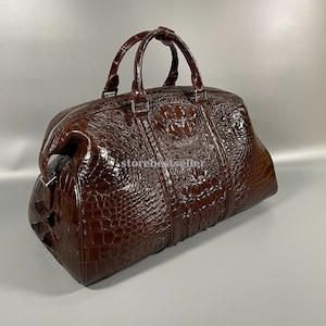 May include: A brown crocodile leather travel bag with a top handle and a zip closure. The bag has a textured crocodile skin pattern.