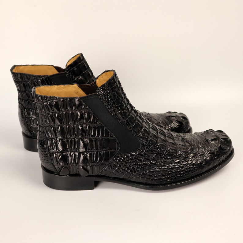 May include: A pair of black leather ankle boots with a crocodile-embossed pattern. The boots have a pointed toe and a low heel.